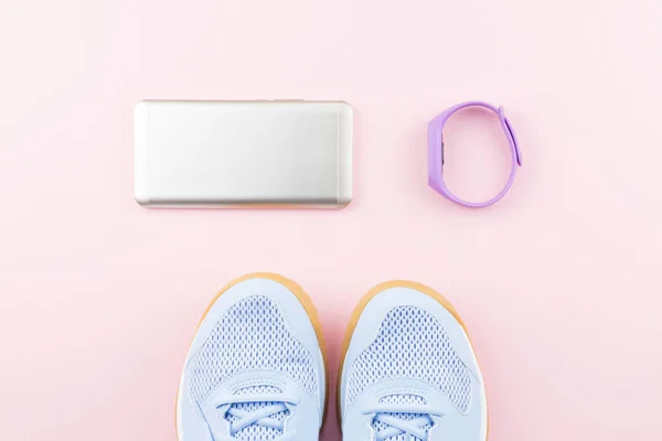 Woman sneakers, fitness tracker and smartphone on pastel pink background. Sport fashion concept. Flat lay