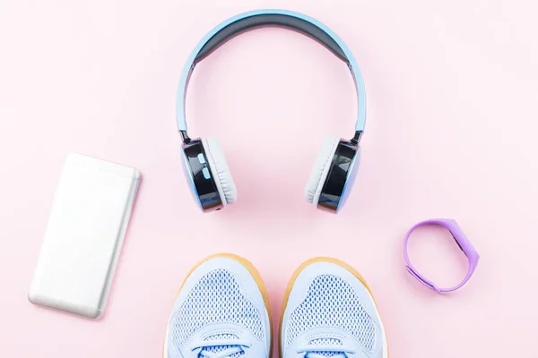 Woman sneakers, headphones, fitness tracker and running clothes on pastel pink background. Sport fashion concept. Flat lay, top view