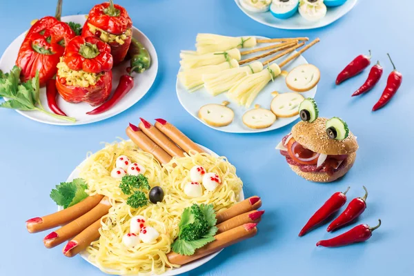 Halloween party food. Stuffed peppers with scary faces, cheese witches brooms, monster hamburgers, witch fingers treats. Top view