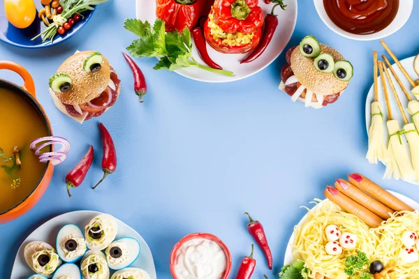 Halloween party food. Stuffed peppers with scary faces, cheese witches brooms, monster hamburgers, witch fingers treats. Top view