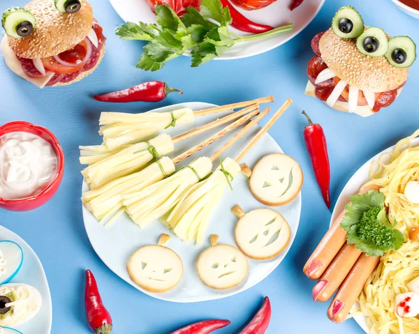 Halloween party food. Stuffed peppers with scary faces, cheese witches brooms, monster hamburgers, witch fingers treats. Top view