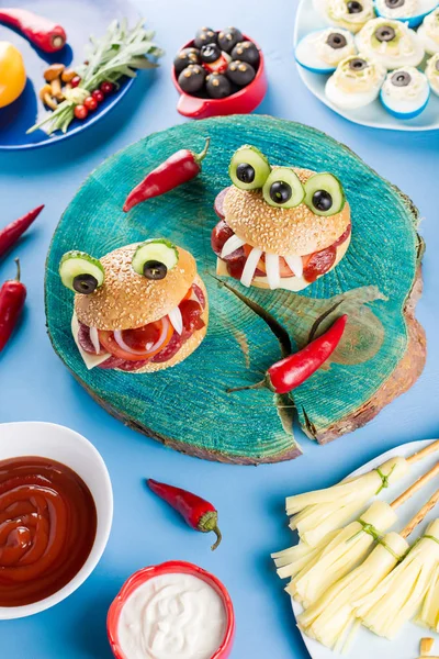 Halloween party food. Stuffed peppers with scary faces, cheese witches brooms, monster hamburgers, witch fingers treats. Top view