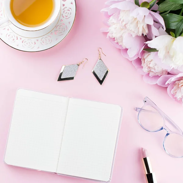 Beautiful cosmetics and flowers flat lay with note book, herbal tea on pastel background.