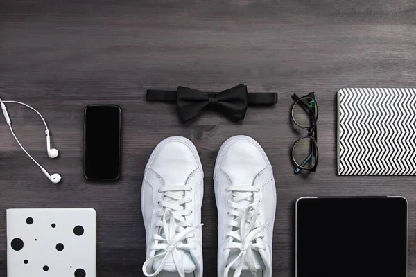 Modern men fashion accessories and electronic devices on dark background. White sneakers, tablet and phone flat lay