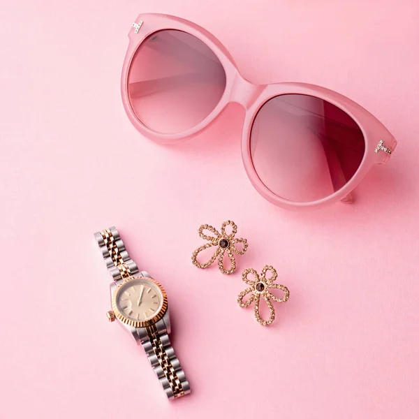 Glamorous woman accessories - watch, sunglasses, earrings. Feminine composition on pink background