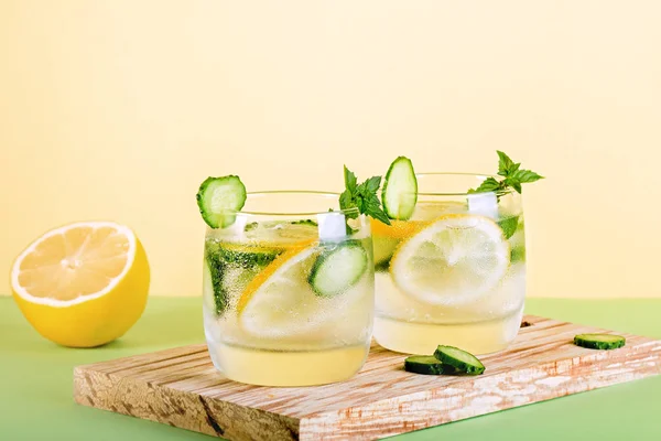 Summer refreshing non alcoholic cocktails with lemon, cucumber and mint, closeup on yellow background