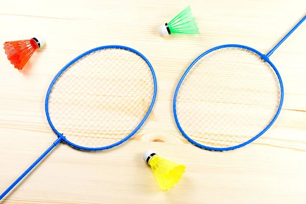 Colorful shuttlecocks and badminton rackets flat lay on wooden desk. Sports and recreation concept