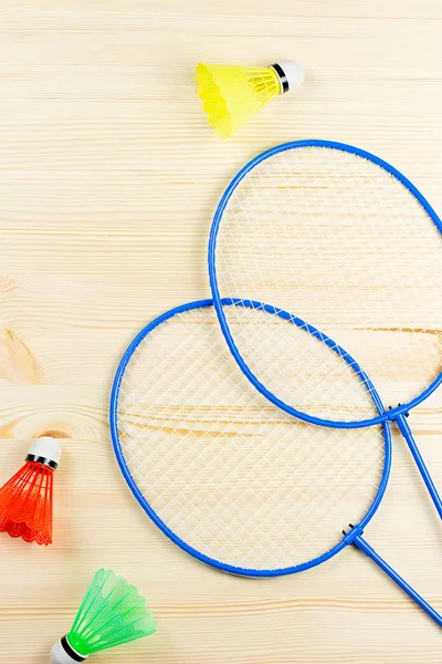 Colorful shuttlecocks and badminton rackets flat lay on wooden desk. Sports and recreation concept