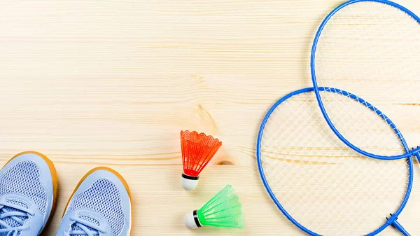 Colorful shuttlecocks and badminton rackets flat lay on wooden desk. Sports and recreation concept