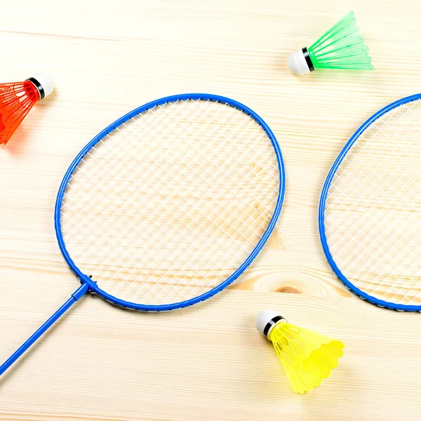 Colorful shuttlecocks and badminton rackets flat lay on wooden desk. Sports and recreation concept