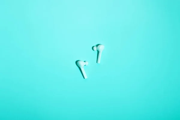 Wireless in ear headphones on blue background close up. Minimal music concept. White earphones flat lay, top view