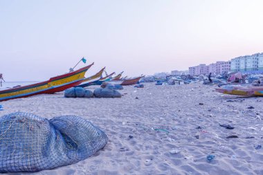 Gün batımında tekneler etrafında balıkçılık ağları ve atık nesneleri ile deniz kıyısında park balıkçı tekneleri, Chennai marina plaj