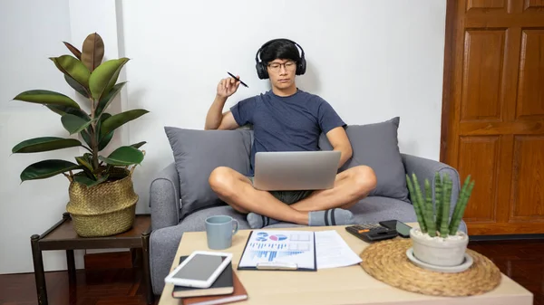 Asian entrepreneur working at home on some project with his laptop at home with paperworks and documents on table in living room, work from home concept