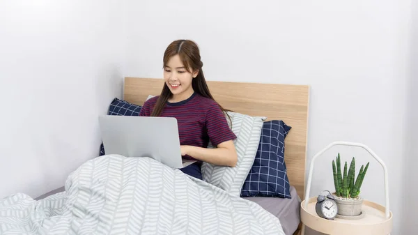 Asian woman using laptop computer on the bed and enjoy working at home, Working remotely or Work from home and concept.