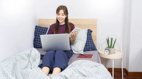 Asian woman using laptop computer on the bed and enjoy working at home, Working remotely or Work from home and concept.