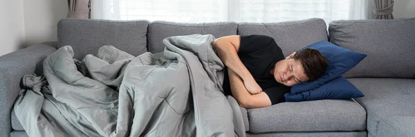 有病和身体不适的亚洲男人把头抬起来 头疼得厉害 睡在家里的沙发上 裹着灰蒙蒙的毛毯 — 图库照片