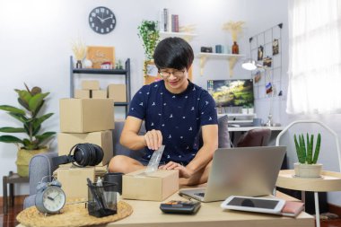 Asyalı erkek işyeri sahibi ya da internet üzerinden merchance satan ve müşteriye sipariş göndermek için ürün paketleme karton paket kutusu hazırlayan, online alışveriş, iş sahibi, teslimat konsepti