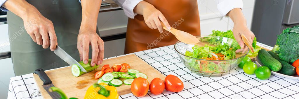 Happy couple having fun standing in kitchen at home preparing vegetable salad husband and wife vegetarians chop vegetables prepare for dinner in loft kitchen at home