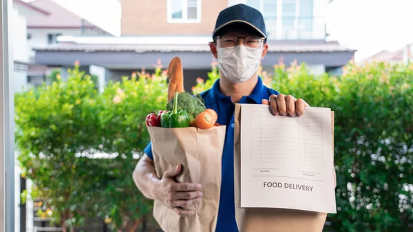 Asian deliver man in uniform with respirator face mask is delivering the paper bag waiting for the customer in front of the home during lockdown, Food delivery service