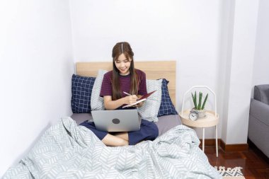 Yatakta dizüstü bilgisayar kullanan Asyalı kadın evde çalışmaktan, uzaktan çalışmaktan ya da evden çalışmaktan keyif alıyor..
