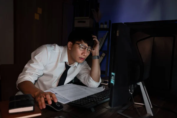 压力很大的年轻亚洲商人一个人在办公室工作到很晚 他的眼睛都要闭上了 看起来很头疼 加班超负荷工作的概念 — 图库照片