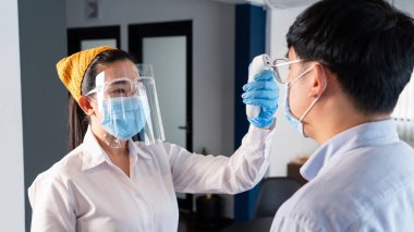 Garson maske takıyor ve alıcıyla müşterinin vücut ısısını kontrol ediyor Coronavirus 'tan korumak için restorana girmeden önce Tıbbi Dijital Kızılötesi Termometre kullanıyor (COVID-19).