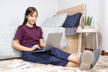 Yatakta dizüstü bilgisayar kullanan Asyalı kadın evde çalışmaktan, uzaktan çalışmaktan ya da evden çalışmaktan keyif alıyor..