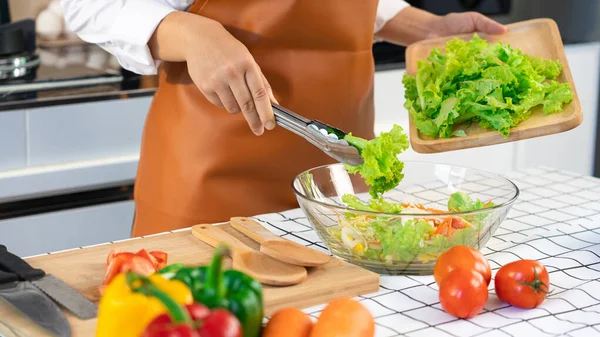 woman in the process of preparing healthy food Vegetable Salad mixing salad wooden spoon in kitchen at home Dieting Concept.
