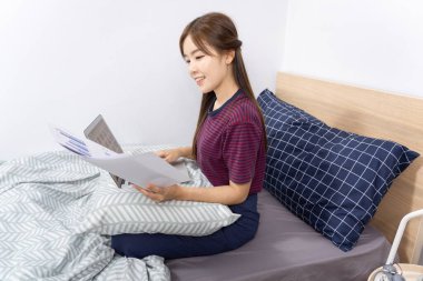 Yatakta dizüstü bilgisayar kullanan Asyalı kadın evde çalışmaktan, uzaktan çalışmaktan ya da evden çalışmaktan keyif alıyor..