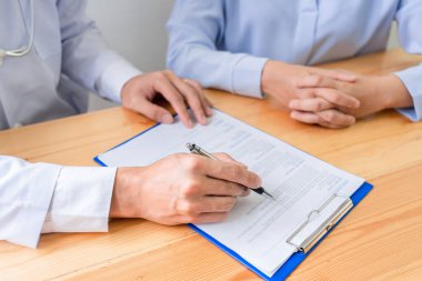 Çekici Asyalı erkek doktor klinikteki bir kadın hastaya tavsiye ve tıbbi danışmanlık yapıyor.