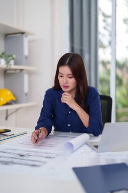 Genç Asyalı kadın mimar titizlikle tasarım planlar odaklanmış profesyonel planlar inşaat projeleri parlak ofis ortamı