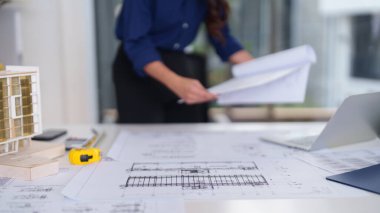 Profesyonel mimar çalışma masasında ayrıntılı bina modelleri ve tasarım araçları sergileniyor. Gelecekteki inşaat projeleri için odaklanmış yaratıcı süreç.