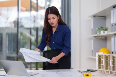 Adanmış Asyalı mimar karmaşık bina planlarını dikkatle inceler. Kentsel gelişim için yenilikçi tasarım çözümleri oluşturmaya odaklanmış profesyonel.