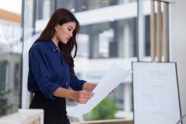 Profesyonel kadın tasarımcı bina planlarını inceler. Çağdaş bir ofis ortamında mimari planlar üzerinde gayretli bir çalışma. Proje geliştirme kavramı.