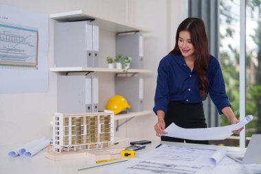 Profesyonel kadın mimar, parlak bir çağdaş çalışma alanı gösterme uzmanlığında ayrıntılı planları ve mimari modeli dikkatle inceliyor.