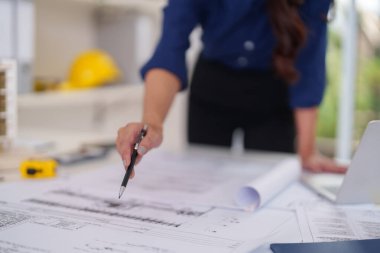 Yetişkin Asyalı kadın mimar bina planlarını inceliyor. Modern bir ofis işyerinde odaklanmış profesyonel iş ayrıntıları.