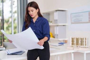 Profesyonel bir ofis ortamında yenilikçi bir kentsel kalkınma projesi için ayrıntılı yapı planları ve tasarım kavramlarını inceleyen odaklanmış Asyalı yetişkin mimar