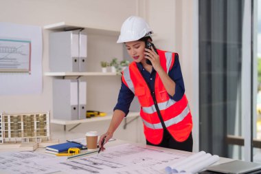 Profesyonel Asyalı kadın mimar, şehir şantiyesindeki bir inşaat ofisindeki telefon yönetimi projeleriyle ilgili tasarım konuşmaları yapıyor..