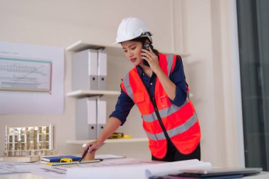 Profesyonel Asyalı yetişkin mimar telefonla iletişim kurar. Bina tasarımı, inşaat projesi yönetimi ve mühendislik çalışmalarını inceledi..