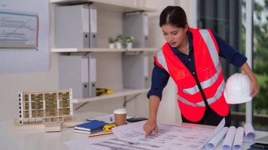 Kendini işine adamış kadın mimar, modern bir ofiste proje başarısını sağlayacak mimari planlar ve modeller üzerinde titizlikle çalışıyor.