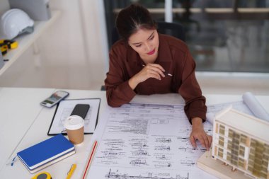 Kadın mimar, ofisinde yeni inşaat kavramları ve yenilikçi yapılar tasarlayan planlar ve ölçekli bir model inceliyor.