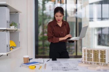 Profesyonel kadın mimar, son inşaat projesinde geliştirdiği dizüstü bilgisayarın mimari planlarını ve modellerini titizlikle inceliyor.