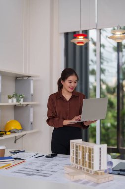 Tasarımlar yapan profesyonel Asyalı mimar kadın. Bir ofis stüdyosunda çalışıyor. Bina planlarını ve şehir projelerini geliştiriyor..