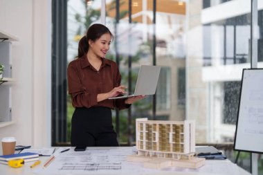 Yetenekli Asyalı mimar kadın modern ofis ortamını kullanarak kentsel gelişim için yenilikçi bina planları geliştiriyor.