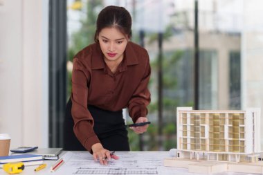 Asyalı kadın mimar, mimari planlar, model ofis, çalışma alanı, modern tasarım projeleri, akıllı teknoloji araçları uzmanlığı ile özenle çalışıyor.