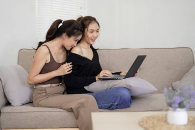 Asyalı kadınlar kanepede dizüstü bilgisayar kullanarak dinlenirler. Samimi anları paylaşıyorlar ve rahat evlerinde dijital olarak bağlanıyorlar. Neşeli modern ortaklık.