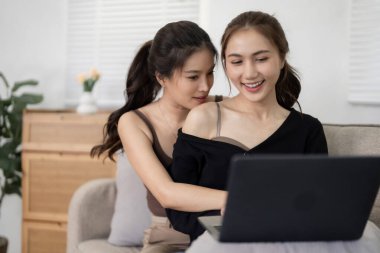 Asyalı yetişkin kadınlar rahat kanepelerinde dizüstü bilgisayarlarını seve seve paylaşırlar. Sevgiyle kucaklaşarak, dijital içeriği keşfediyorlar. Samimi bağlantı, rahat konfor.