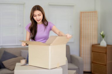 Asyalı kadın sevinçle bir karton kutuyu açıyor. Yeni dairesindeki eşyaları açıyor. Gündüz yerleşim yerinin yerleşim yerinin aktivitesini düzenliyor.