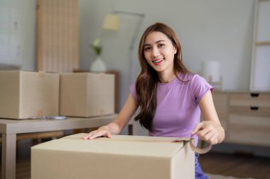 Genç Asyalı kadın yeni bir eve ya da daireye taşınmaya hazırlanıyor. Eşyalarını karton kutulara doldurup evinde bantla kapatıyor..