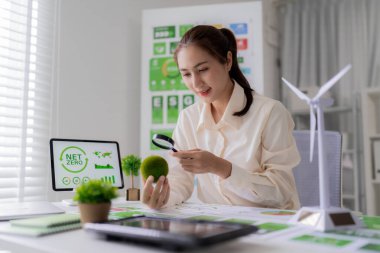 Asyalı kadın, ofisteki sürdürülebilir iş uygulamalarını teşvik eden sosyal yönetim için büyüteç kullanarak net sıfır etkisini inceliyor..